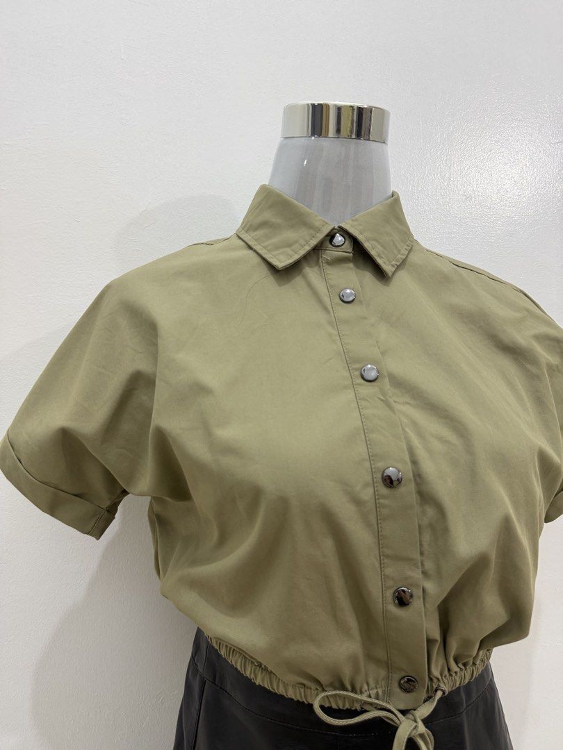Olive Green Cropped Button-Up Shirt with Drawstring Waist (Category: Shirts) located in Manila. Submitted by e.louise (Listing ID 1464334820, Image 2). Description: - Olive green cropped shirt - Short sleeves with rolled cuffs - Collared neckline with button-up front - Adjustable drawstring hem - Versatile for pairing with high-waisted bottoms - Comfortable and stylish for casual outfits.