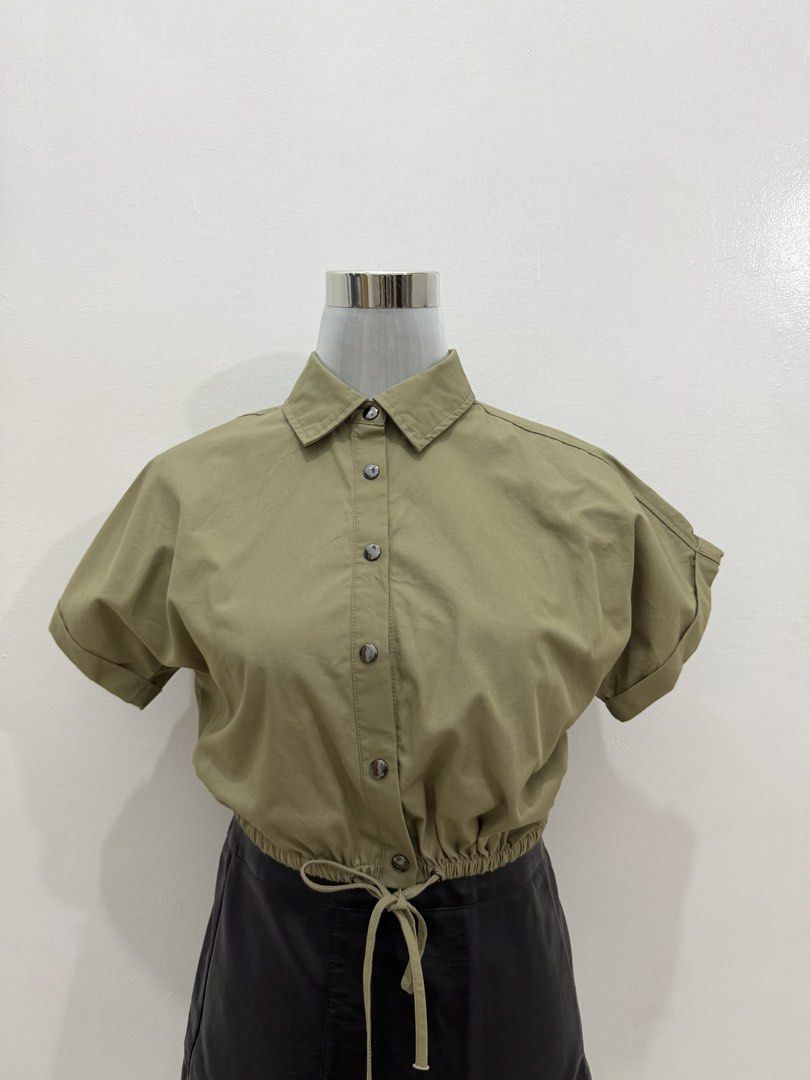 Olive Green Cropped Button-Up Shirt with Drawstring Waist (Category: Shirts) located in Manila. Submitted by e.louise (Listing ID 1464334820, Image 1). Description: - Olive green cropped shirt - Short sleeves with rolled cuffs - Collared neckline with button-up front - Adjustable drawstring hem - Versatile for pairing with high-waisted bottoms - Comfortable and stylish for casual outfits.