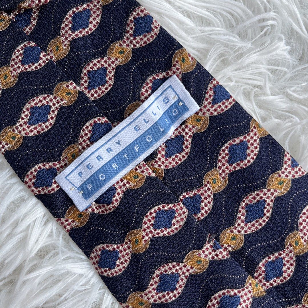 Perry Ellis Portfolio Navy Blue Geometric Pattern Silk Tie (Category: Ties) located in Cuyapo. Submitted by Ashtyn.Pre.Loved (Listing ID 1464256282, Image 2). Description: - Classic navy blue tie from Perry Ellis Portfolio. - Features a repeating geometric pattern in gold, red, and blue. - Made of 100% silk. - Ideal for formal events and business attire. - Elevates any suit with a touch of sophistication..
