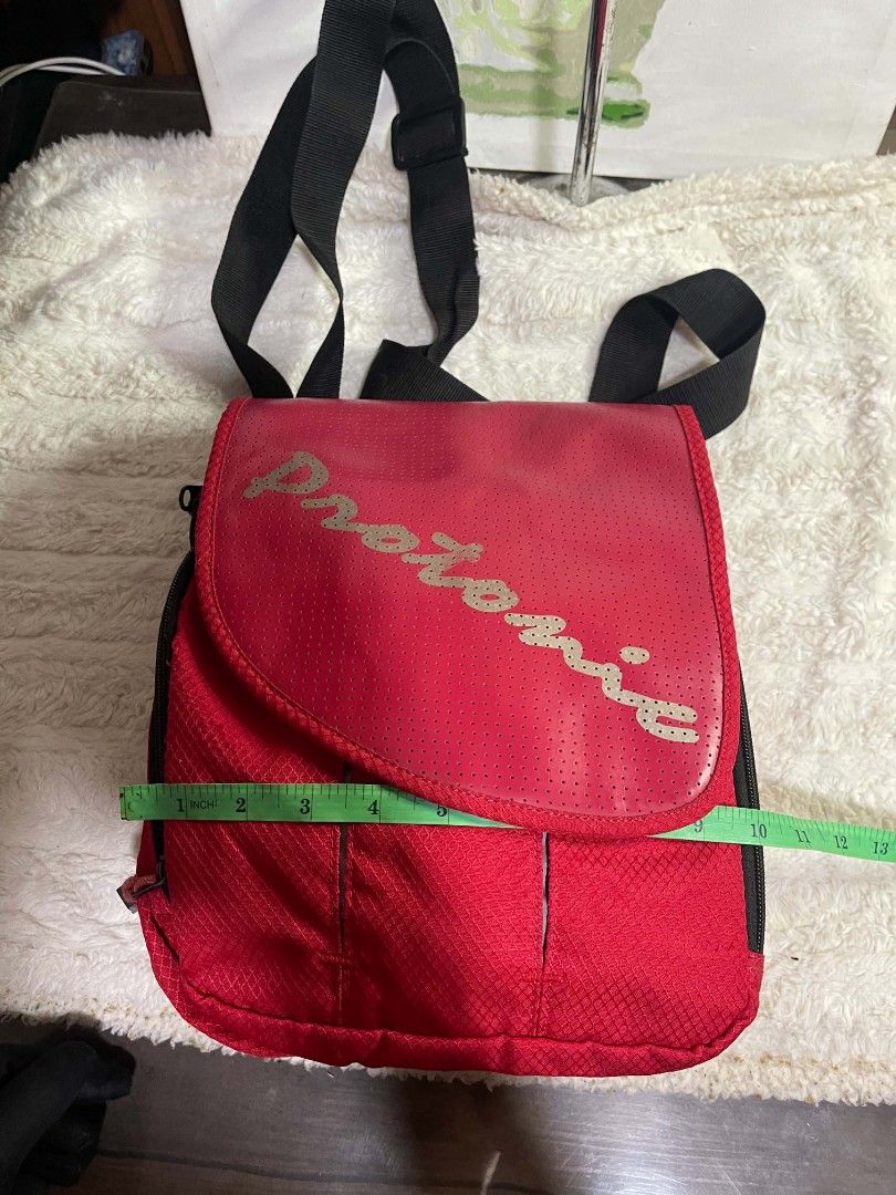 Protonic Red Perforated Backpack Bag (Category: Sling Bags) located in Naawan. Submitted by twilly.apparel2 (Listing ID 1464345339, Image 3). Description: - Stylish red Protonic backpack - Unique perforated front flap with silver lettering - Spacious main compartment with internal pockets - Comfortable adjustable black straps - Ideal for everyday use or travel adventures - Dimensions: Approximately 13 inches tall and 11 inches wide.