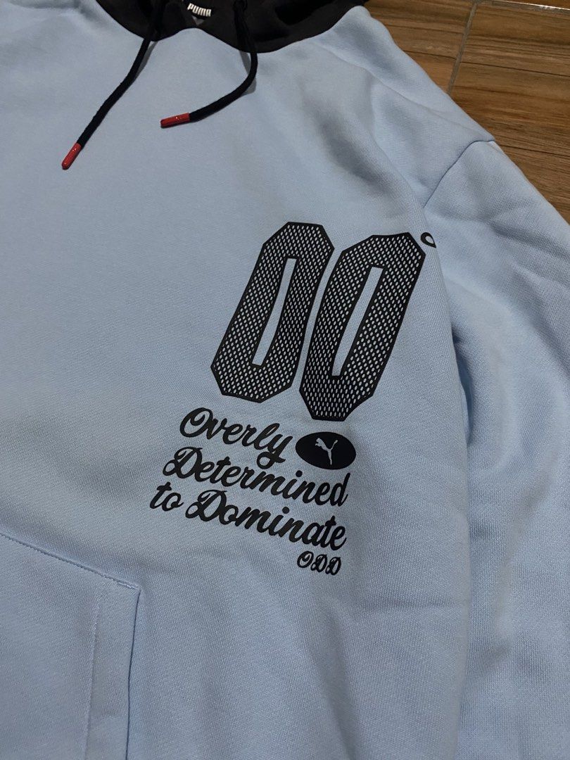 Puma Light Blue "00" Graphic Hoodie (Category: Hoodies) located in Baguio. Submitted by arenzu (Listing ID 1464302743, Image 2). Description: - Light blue Puma hoodie with black accents. - Features a '00' graphic and 'Overly Determined to Dominate' text on the front. - Checkerboard pattern on sleeves and hood. - Puma logo detail on the back. - Includes drawstring hood and a convenient front pocket..