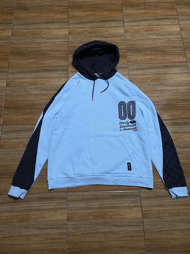 Puma Light Blue "00" Graphic Hoodie (Category: Hoodies) located in Baguio. Submitted by arenzu (Listing ID 1464302743, Image 1). Description: - Light blue Puma hoodie with black accents. - Features a '00' graphic and 'Overly Determined to Dominate' text on the front. - Checkerboard pattern on sleeves and hood. - Puma logo detail on the back. - Includes drawstring hood and a convenient front pocket..