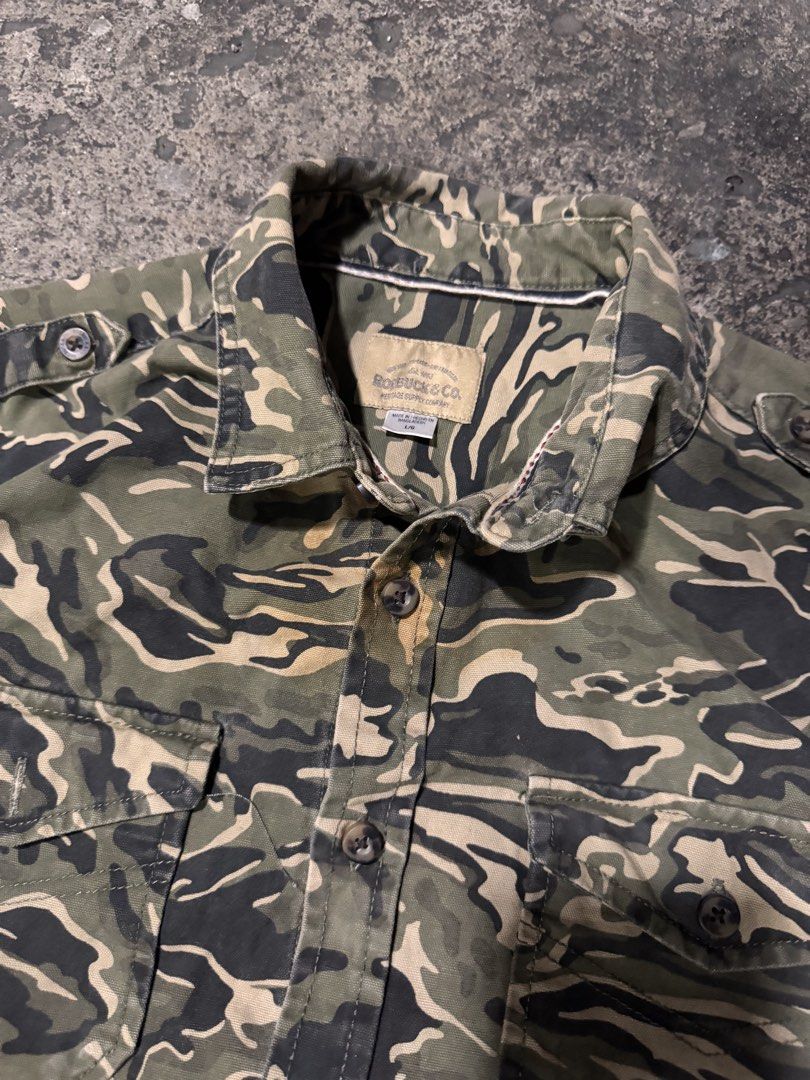 Roebuck & Co. Camouflage Button-Up Shirt (Category: Tshirts & Polo Shirts ) located in Pasig City. Submitted by dripthrift1600 (Listing ID 1464247420, Image 3). Description: - Brand: Rocawear & Co. - Style: Camouflage button-up shirt - Sleeves: Long sleeves with button cuffs - Pockets: Two chest pockets with button closures - Closure: Button-down front - Occasion: Great for casual wear - Condition: Please check photos for details - Dimes: 23x28.