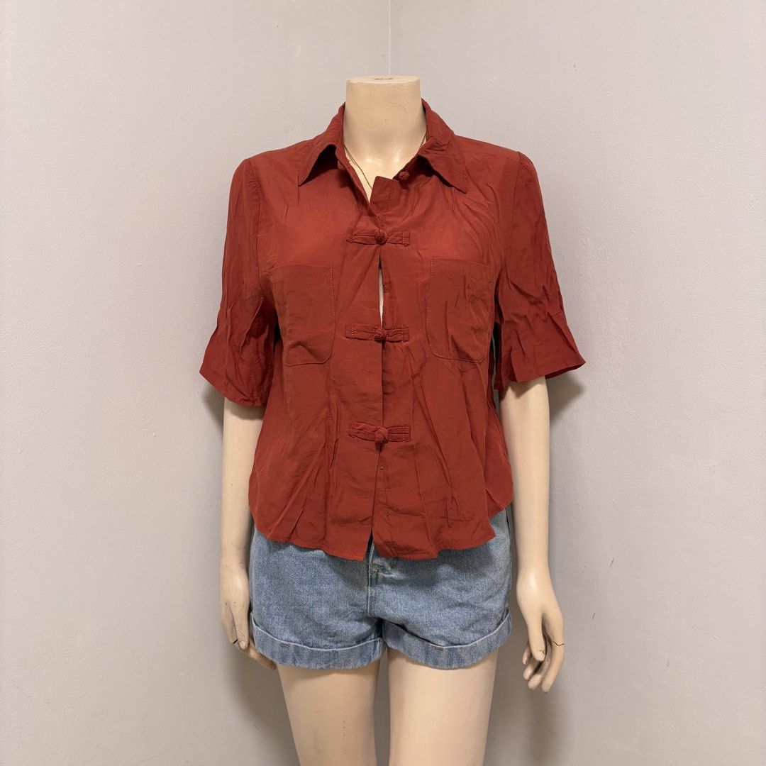 Rust Mandarin Collar Blouse (Category: Blouses) located in Imus. Submitted by reloved.nd (Listing ID 1464261023, Image 1). Description: - Vibrant orange shirt - Stylish mandarin collar - Unique frog button closures down the front - Short sleeves with a subtle flare - Two convenient chest pockets - Fabric with a pleasing subtle texture - Versatile: pairs perfectly with shorts or jeans.