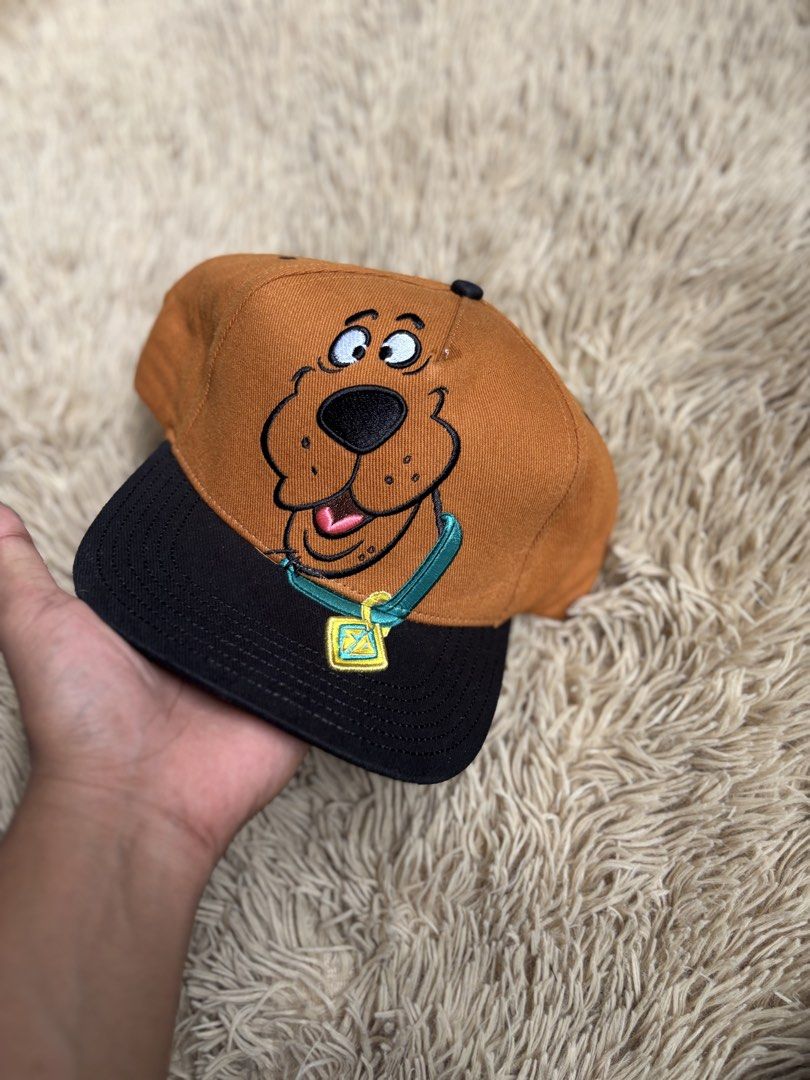 Scooby-Doo Embroidered Snapback Cap (Category: Caps & Hats) located in Quezon City. Submitted by nojthrift (Listing ID 1464251835, Image 2). Description: - Brown and black snapback cap - Features embroidered Scooby-Doo face and iconic tag - Adjustable strap at the back - Ideal for Scooby-Doo fans - Fun accessory for casual outfits.