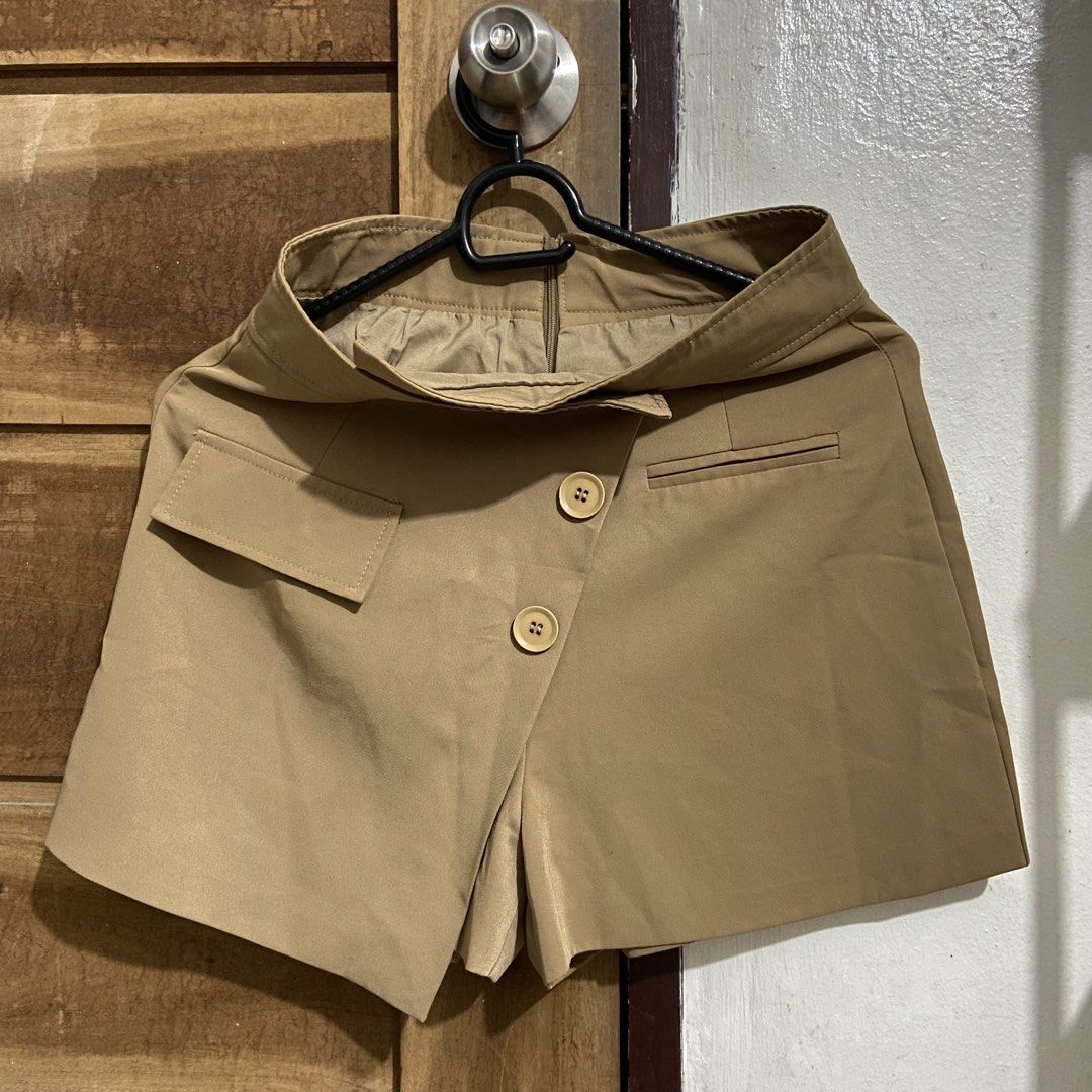 Tan Asymmetrical Button Skort (Category: Shorts) located in Valenzuela. Submitted by _1011100 (Listing ID 1464285929, Image 1). Description: - Tan skort with a skirt-like appearance and built-in shorts. - Asymmetrical button closure for a stylish detail. - Functional pocket on the left side. - Faux pocket on the right side. - Elastic waistband ensures a comfortable and flexible fit. - Ideal for creating a chic and casual outfit..