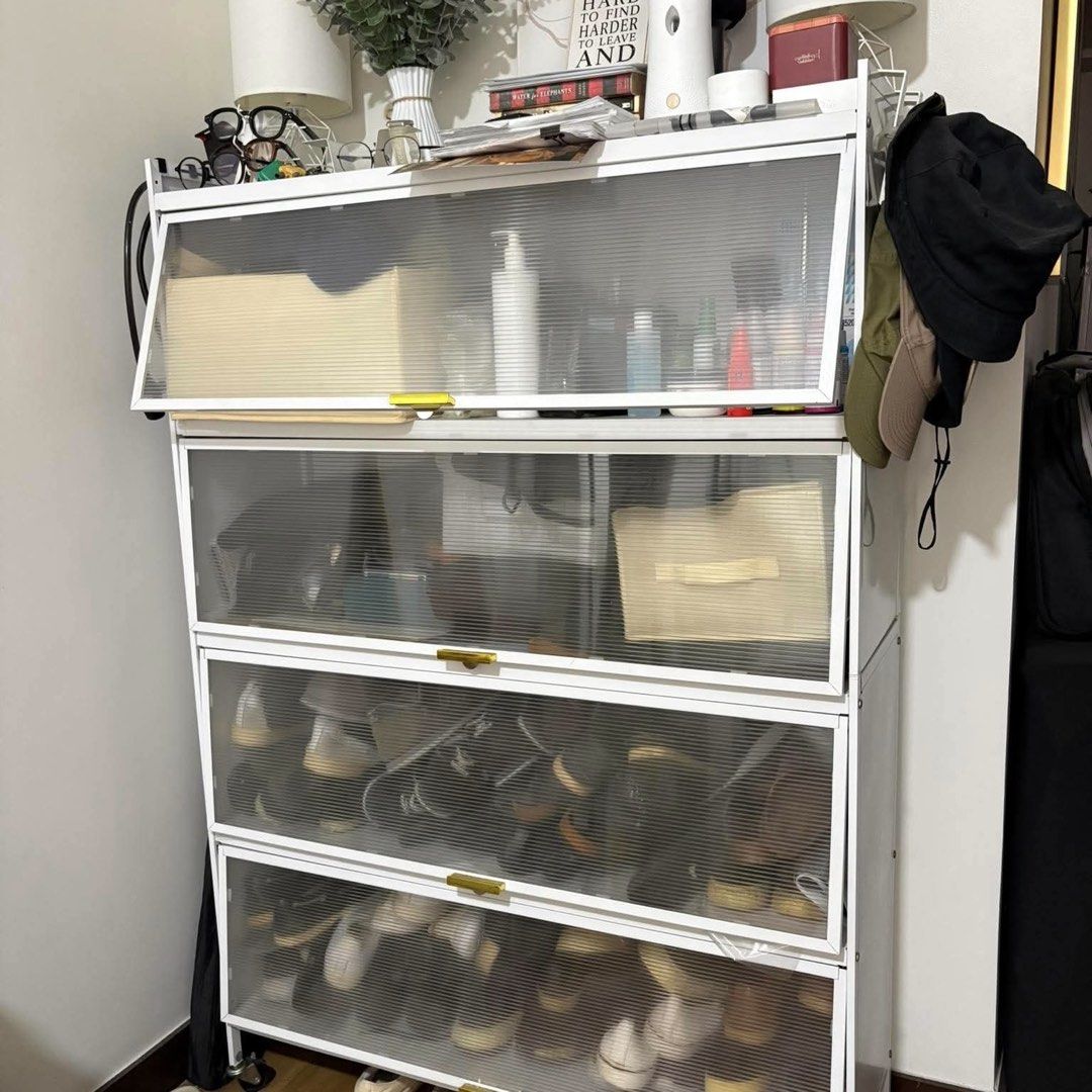 White 4-Tier Shoe Rack with Transparent Doors (Category: Shelves, Cabinets & Racks) located in Paranaque City. Submitted by 903101 (Listing ID 1464226753, Image 1). Description: - White 4-tier shoe rack - Features transparent doors with elegant gold handles - Ideal for organizing shoes, bags, or other household items - Provides a practical and stylish storage solution for any room - Top shelf includes a decorative box and bottles (for display pur