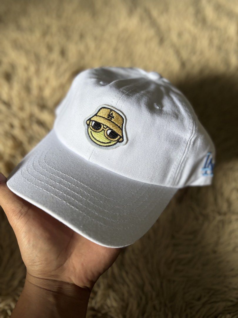 White LA Dodgers Baseball Cap with Fun Patch (Category: Caps & Hats) located in Quezon City. Submitted by nojthrift (Listing ID 1464251067, Image 2). Description: - White baseball cap - Features a cool embroidered smiley face patch (wearing a bucket hat and sunglasses) - LA Dodgers logo embroidered on the side - Adjustable strap at the back for a comfortable fit - Ideal for casual outfits and showing your team spirit.