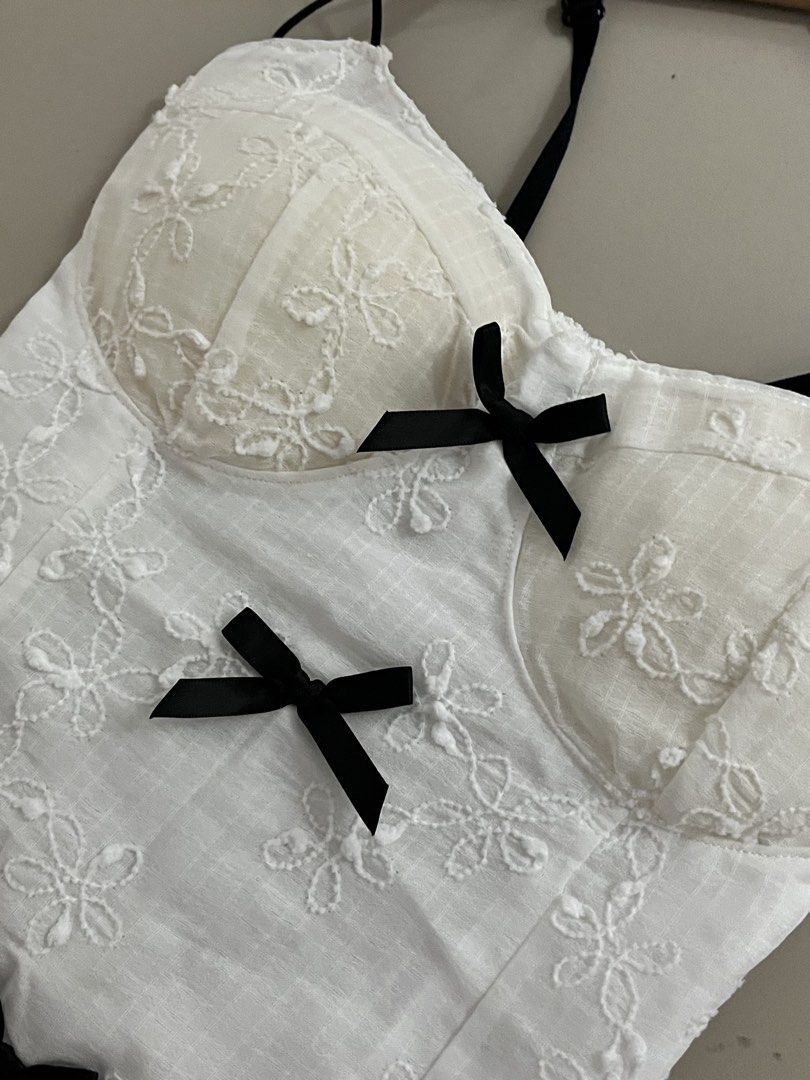 White Lace Corset Top with Black Bows (Category: Sleeveless) located in Orion. Submitted by sofqzh (Listing ID 1464227591, Image 2). Description: - White lace corset top - All-over embroidered floral details - Adjustable black straps - Three black bows down the front - Structured cups - Pairs well with jeans or skirts - Ideal for nights out or special occasions Shuojo, cottage core, soft fairy core, cool girl.