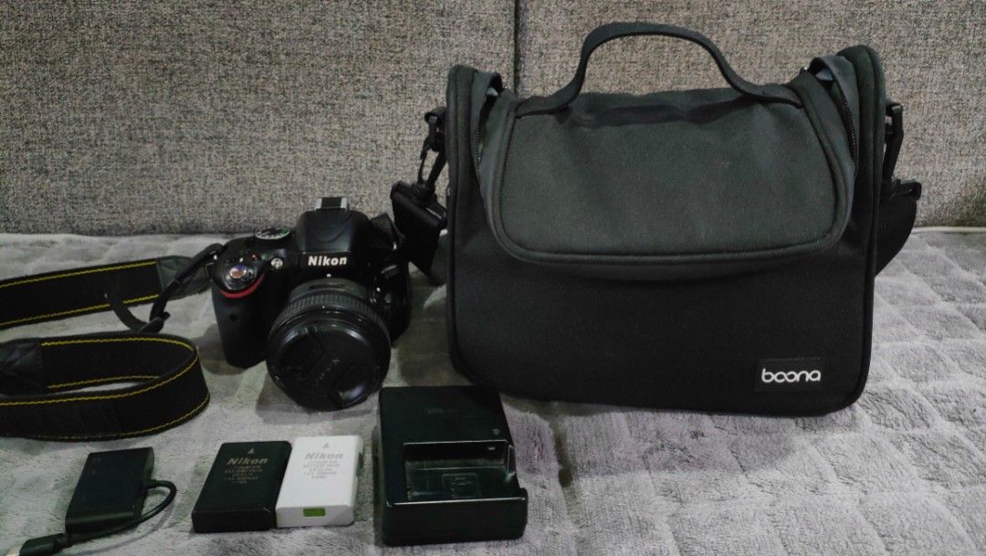 50mm Nikon D5100 DSLR Camera and Accessories (Category: Cameras) located in Taguig. Submitted by fundraising_for_althon (Listing ID 1422393745, Image 1). Description: Includes a Nikon D5100 DSLR camera body, 50mm lense, two batteries, a charger, a memory card, lens caps, and a camera bag. The camera bag has multiple compartments. Also includes a drawstring pouch.