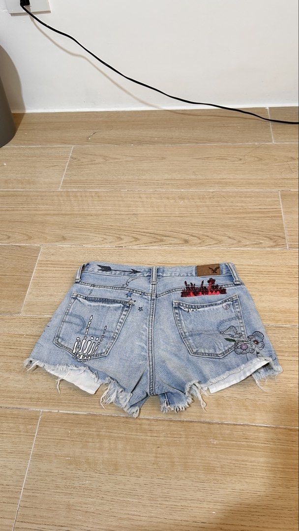 American Eagle Distressed Denim Shorts with Custom Patches (Category: Shorts) located in San Mateo. Submitted by maxxysclosetclearout (Listing ID 1464375286, Image 2). Description: - Brand: American Eagle - Wash: Light wash denim - Details: Distressed, raw hem - Unique Feature: Custom patches on back pockets (skeleton hands, floral designs) - Style: Edgy, casual - Pairing Suggestion: Great with a simple top.