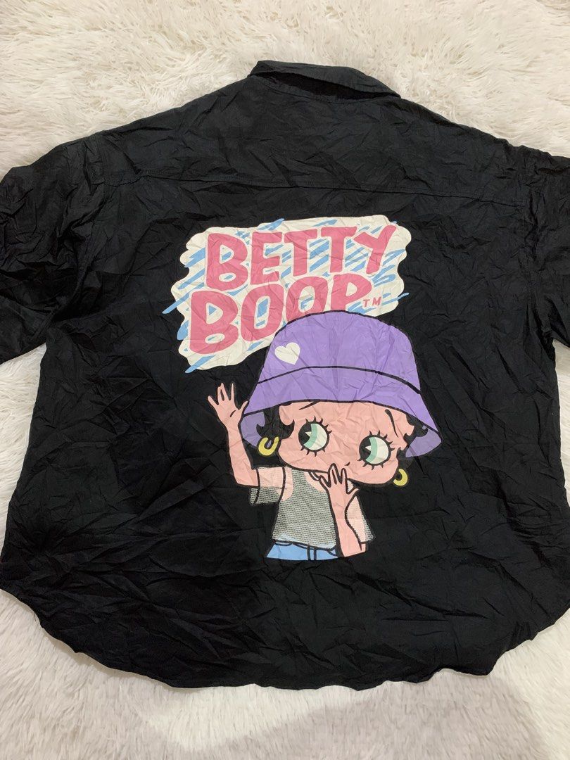 Betty Boop Black Button Up Shirt (Category: Shirts) located in Iba. Submitted by thriftcoyan (Listing ID 1464446069, Image 3). Description: - Black button-up shirt - Short sleeves -Dimes: 25x27 -Best fit large - Betty Boop graphic on the back - Small bucket hat graphic on the front left chest - Brand: Betty Boop.