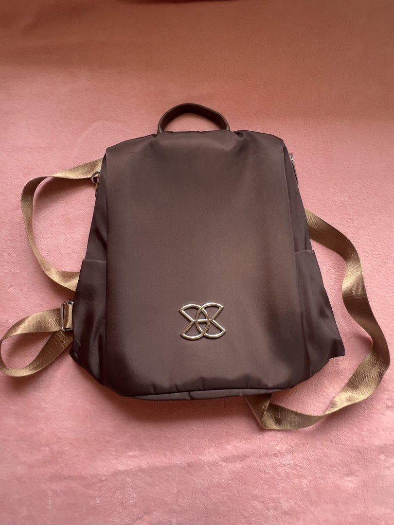 Brown Nylon Backpack with Gold Accents (Category: Backpacks) located in Batangas. Submitted by alaisaampa7513 (Listing ID 1464569885, Image 1). Description: - Durable brown nylon backpack - Convenient front zip pocket - Handy side pockets for easy access - Spacious main compartment with internal organization pockets - Adjustable straps for a comfortable fit - Stylish gold logo accent on the front - Ideal for everyday adventures and errands.