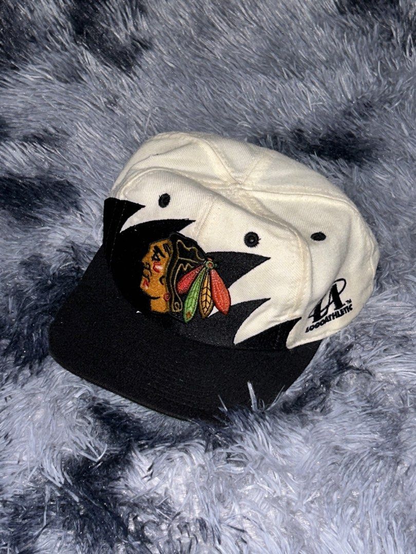 Chicago 90s Blackhawks Sharktooth Logo Athletic Cap (Category: Caps & Hats) located in Cadiz. Submitted by jaybatiller (Listing ID 1464384808, Image 1). Description: - Vintage Chicago Blackhawks cap - Classic Blackhawks logo on front - Black brim and white crown - Logo Athletic branding on side - Adjustable strap for a custom fit - Shows some signs of wear, adding to its vintage charm - Perfect for any Blackhawks fan!.