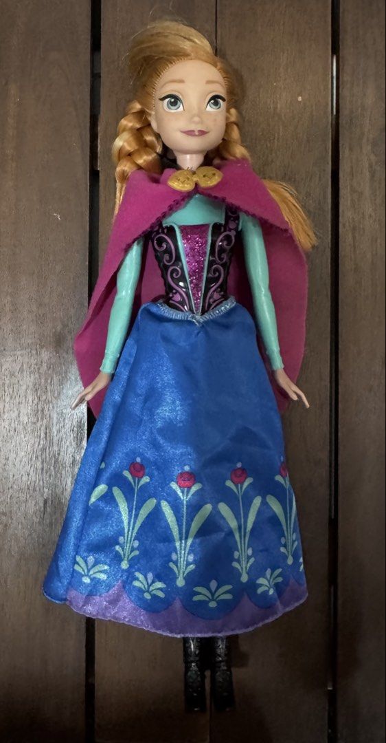 Disney Frozen Anna Doll (Category: Kids Toys) located in Quezon City. Submitted by kcapi (Listing ID 1464409178, Image 1). Description: - Anna doll from Disney's Frozen - Features signature braided blonde hair - Wears iconic blue and purple dress with floral pattern - Includes a pink cape.