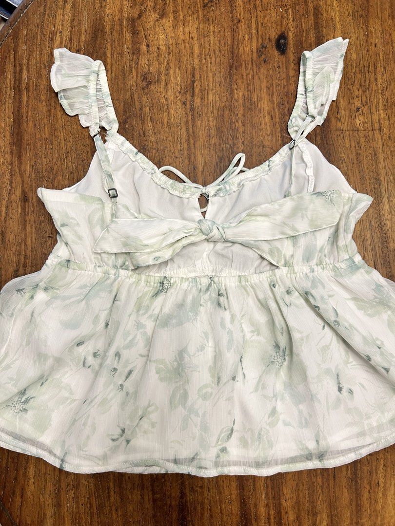 Hollister Top (Category: Sleeveless) located in Manila. Submitted by tshopph (Listing ID 1464368703, Image 2). Description: Floral Ruffle Strap Cami Top 🌸🌿 Super pretty and feminine floral cami top! Perfect for brunch dates, casual outings, picnics, or beach trips ✨ Color / Pattern: White with a subtle, soft sage green floral print ✨ Neckline & Front: Sweetheart-style bust with a small keyhole cutout and front tie detail ✨ Straps: Cute ruffled 