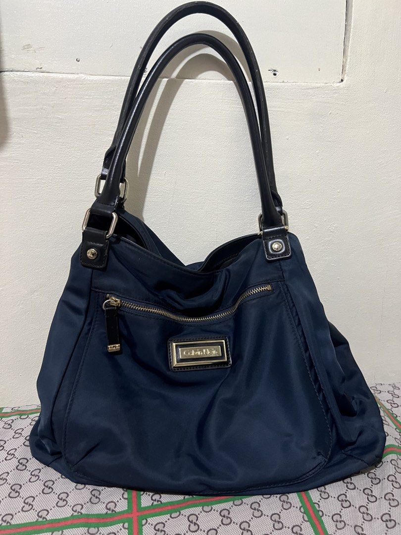 Preloved Calvin Klein hobo nylon bag (Category: Luxury Bags & Wallets) located in Makati City. Submitted by transactwithme (Listing ID 1464466143, Image 1). Description: Preloved Calvin Klein shoulder bag Not abused, hardwares can be seen a slight changesi in color but overall still in very good condition Color: navy blue Material: nylon Size H 28 L 35 W 12 .