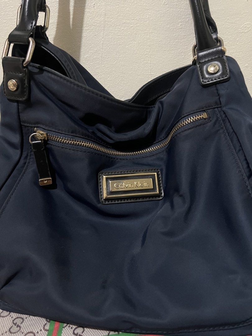 Preloved Calvin Klein hobo nylon bag (Category: Luxury Bags & Wallets) located in Makati City. Submitted by transactwithme (Listing ID 1464466143, Image 2). Description: Preloved Calvin Klein shoulder bag Not abused, hardwares can be seen a slight changesi in color but overall still in very good condition Color: navy blue Material: nylon Size H 28 L 35 W 12 .