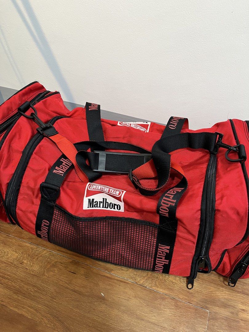 Red Marlboro Adventure Team Duffle Bag (Category: Sling Bags) located in Baao. Submitted by plainclothesdept (Listing ID 1464528039, Image 3). Description: Marlboro Duffle Bag height - 12 in. width - 12 in. length - 28 in. capacity - 66 liters signs of wear 2450 - Vintage Marlboro Adventure Team duffel bag - Bright red with black accents - Spacious main compartment - Side mesh pockets - Front zip pocket - Durable straps and handles - Ideal for tr