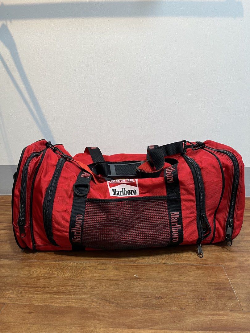 Red Marlboro Adventure Team Duffle Bag (Category: Sling Bags) located in Baao. Submitted by plainclothesdept (Listing ID 1464528039, Image 2). Description: Marlboro Duffle Bag height - 12 in. width - 12 in. length - 28 in. capacity - 66 liters signs of wear 2450 - Vintage Marlboro Adventure Team duffel bag - Bright red with black accents - Spacious main compartment - Side mesh pockets - Front zip pocket - Durable straps and handles - Ideal for tr