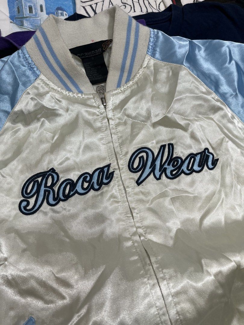 Roca Wear Satin Bomber Jacket (Category: Coats, Jackets and Outerwear) located in Baao. Submitted by plainclothesdept (Listing ID 1464533331, Image 2). Description: Roca Wear Bomber Jacket width - 21 in. length - 22 in. few stains - Cool Roca Wear satin bomber jacket - White body with light blue sleeves and trim - Embroidered Roca Wear logo on the front - Ribbed collar, cuffs, and hem - Two front pockets - Perfect for layering or as a statement p