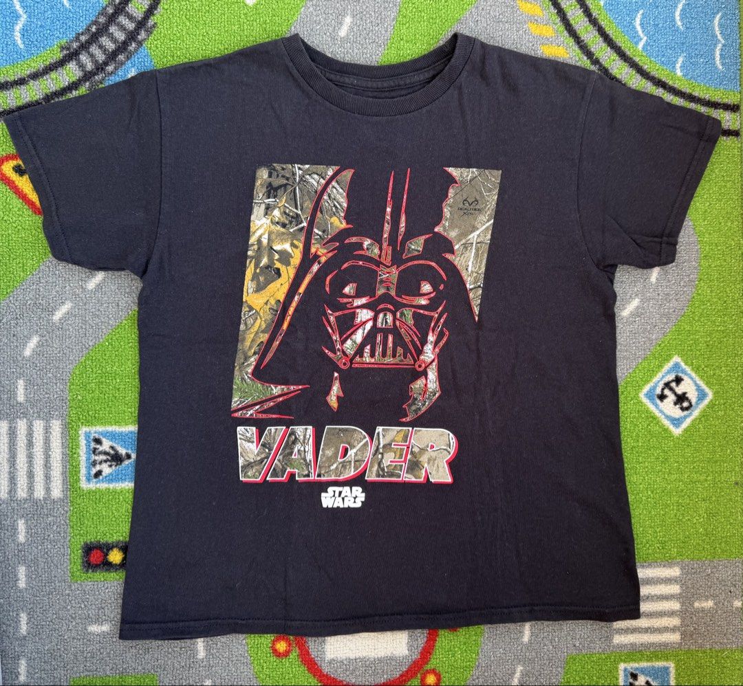 Star Wars Darth Vader Camo Shirt (Category: Babies & Kids Fashion) located in Rizal. Submitted by preloovved (Listing ID 1464474261, Image 1). Description: Cool black t-shirt featuring a Darth Vader graphic with Real Tree camo fill and 'VADER' text. Perfect for Star Wars fans, ideal for casual wear. Preloved, 8yo on tag pero big size, pwede until 10yo if petite Meet-up only in GB1 San Mateo, Rizal Shipping fee c/o buyer. Tres Marias or J&T expres