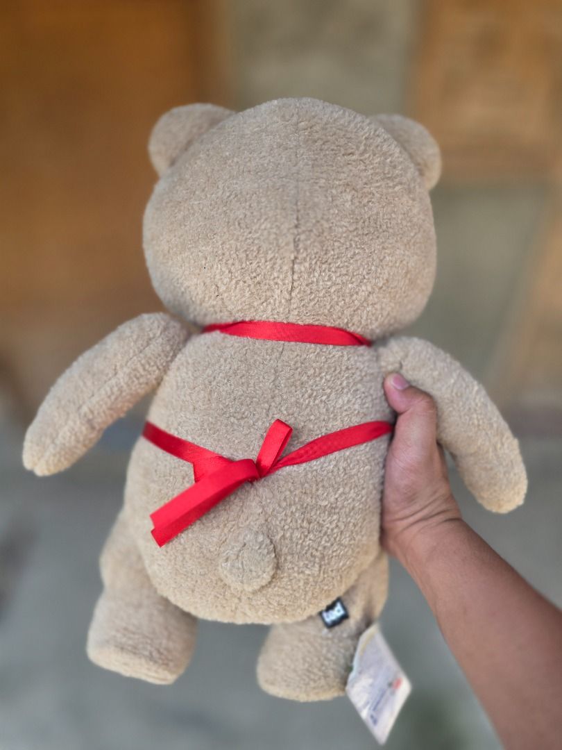 Ted Plush Toy with Red Apron and "Help" Button (Category: Plushies & Soft Toys) located in Santa Maria. Submitted by purefalcon-f7cf (Listing ID 1464362341, Image 3). Description: - Cute Ted plush toy - Original tag still attached - Wearing a red apron with 'Bay Colony Today' name tag - Features a 'How May We Help You Today?' button - Red ribbon tied in a bow on the back - Great for Ted movie fans or as a collectible.