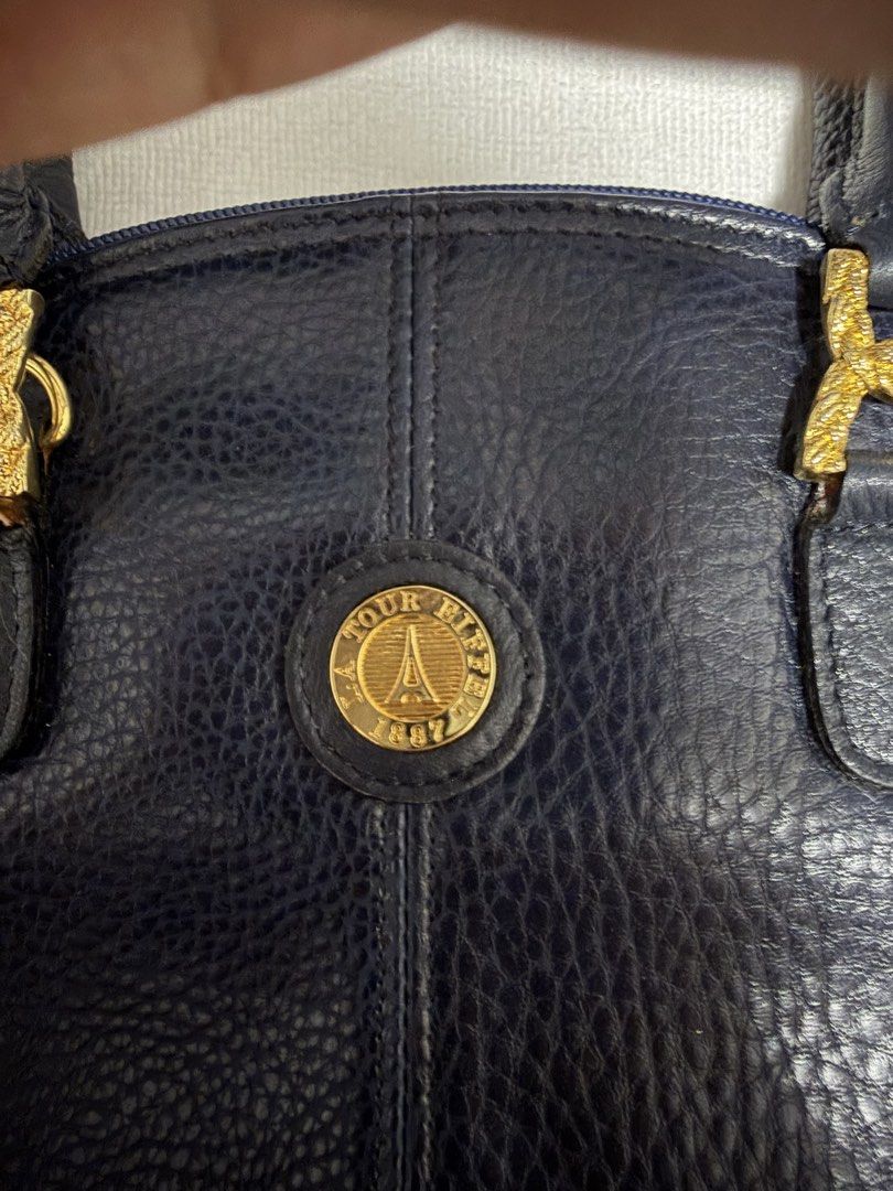 Tour Eiffel 1887 Navy Leather Dome Handbag (Category: Luxury Bags & Wallets) located in Digos. Submitted by old_soul. (Listing ID 1464497389, Image 2). Description: - Navy blue leather dome handbag - Gold-tone hardware with Tour Eiffel 1887 emblem - Secure zipper closure with branded pulls - Adorable small pink and green leather accents - Comfortable top handles for carrying Issue: Inside is cracking .