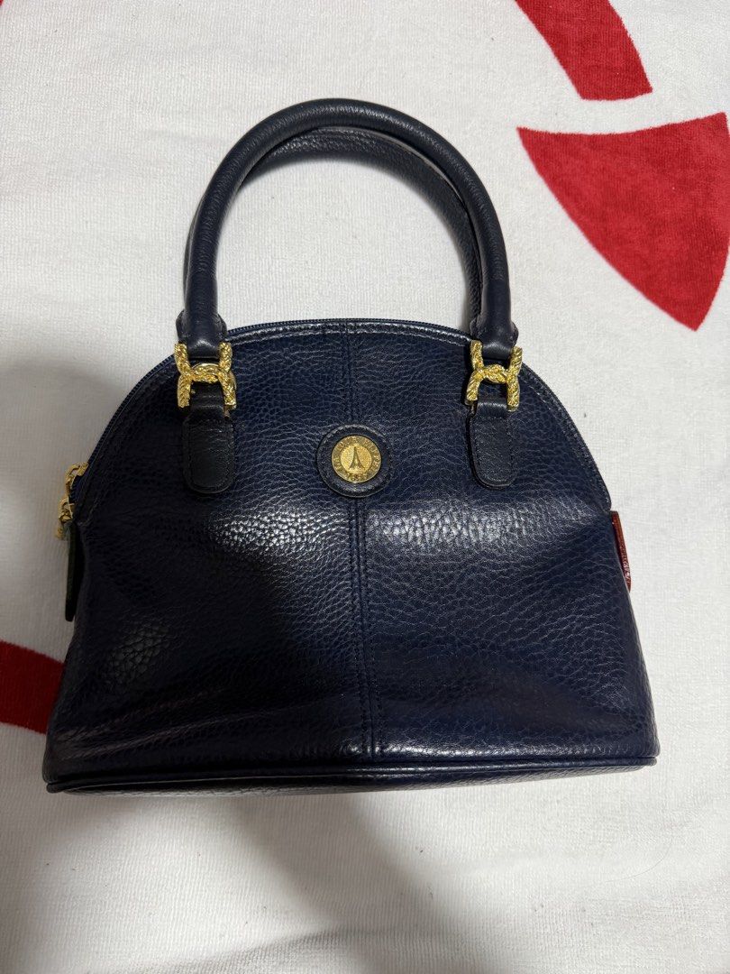 Tour Eiffel 1887 Navy Leather Dome Handbag (Category: Luxury Bags & Wallets) located in Digos. Submitted by old_soul. (Listing ID 1464497389, Image 1). Description: - Navy blue leather dome handbag - Gold-tone hardware with Tour Eiffel 1887 emblem - Secure zipper closure with branded pulls - Adorable small pink and green leather accents - Comfortable top handles for carrying Issue: Inside is cracking .