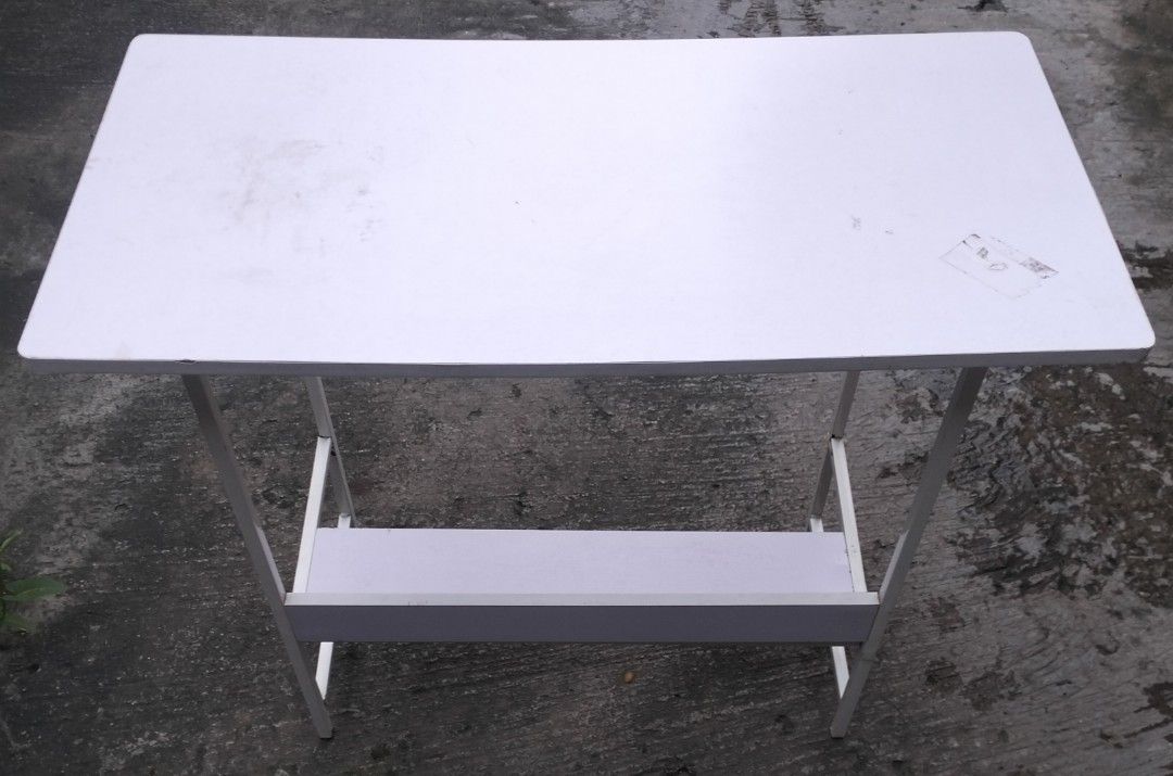 White Table with Shelf (Category: Tables & Sets) located in Bacoor. Submitted by biala17 (Listing ID 1464540890, Image 1). Description: - White table - Features a shelf underneath for extra storage - Metal legs - Top surface has some light marks - Ideal for small spaces or as a temporary desk.