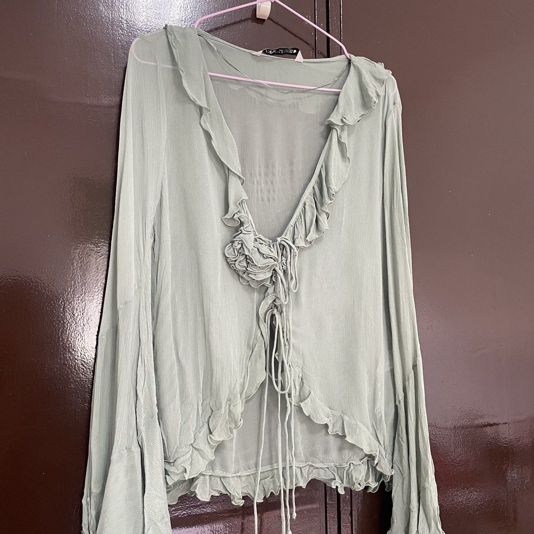 Zara Sheer Ruffle Tie Front Long Sleeve Blouse (Category: Longsleeves) located in Pasay City. Submitted by lovedbyzea (Listing ID 1464537513, Image 2). Description: - with minor flaw on the string (unnoticeable; please see photos) - Light green sheer blouse from Zara - Ruffled neckline and hem - Long bell sleeves - Tie front closure - Decorative floral detail at bust - Lightweight and flowy material - Perfect for layering or wearing alone.