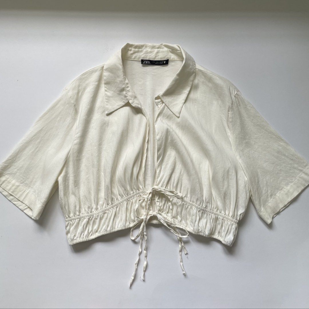 Zara White Cropped Shirt with Drawstring (Category: Shirts) located in Pasay City. Submitted by lovedbyzea (Listing ID 1464537007, Image 1). Description: - can fit Med to Large - White cropped shirt from Zara - Collared neckline and short sleeves - Drawstring detail at the hem to cinch the waist - Can be worn open or tied - Perfect for pairing with high-waisted bottoms - Easy to style for casual or dressed-up outfits.