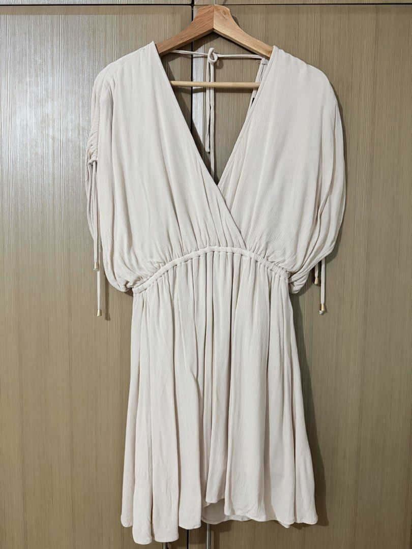 Aakaa Beige V-Neck Dress Size S (Category: Dresses) located in Manila. Submitted by mengxir20193848 (Listing ID 1464709869, Image 1). Description: - Brand: Aakaa - Size: S - Color: Beige - Style: V-neck wrap dress with ruched waist and shoulders - Sleeves: Short sleeves with metallic gold hardware accents on ties - Fabric: Soft, lightweight crinkle texture - Condition: Great for casual outings and warm weather Never used, 100% new.