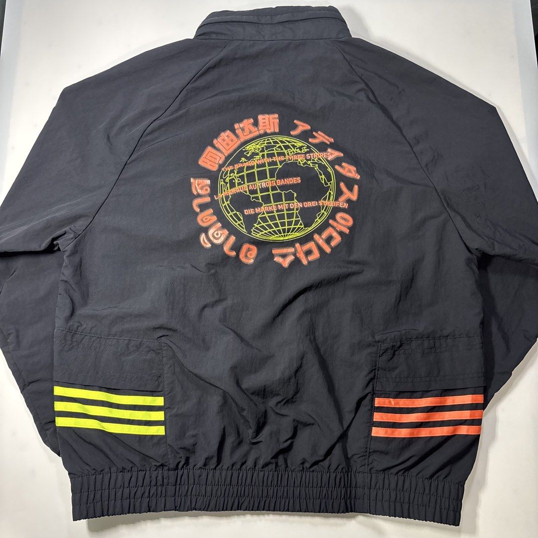 Adidas trefoil track / wind breaker jacket (Category: Coats, Jackets and Outerwear) located in Cavite. Submitted by sidirvinp76902 (Listing ID 1464748316, Image 3). Description: - Brand: Adidas - Color: Black with neon orange and yellow accents - Features: Packable hood, embroidered Trefoil logo on chest, large globe graphic with global text branding on the back - Pockets: Front pockets with vibrant striping - Closure & Fit: Full zip closure, ela