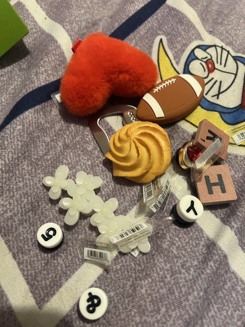 Assorted Crocs Jibbitz charms bundle with box (Category: Designer & Blind Box Toys) located in Quezon City. Submitted by chloesantiago (Listing ID 1464718001, Image 2). Description: - Bundle of assorted Crocs Jibbitz charms - Includes fuzzy red heart, football, yellow cookie, scrabble tiles, white flowers, and number/letter charms - Some charms still attached to original plastic packaging - Stored inside a green Crocs box - Great way to mix and m