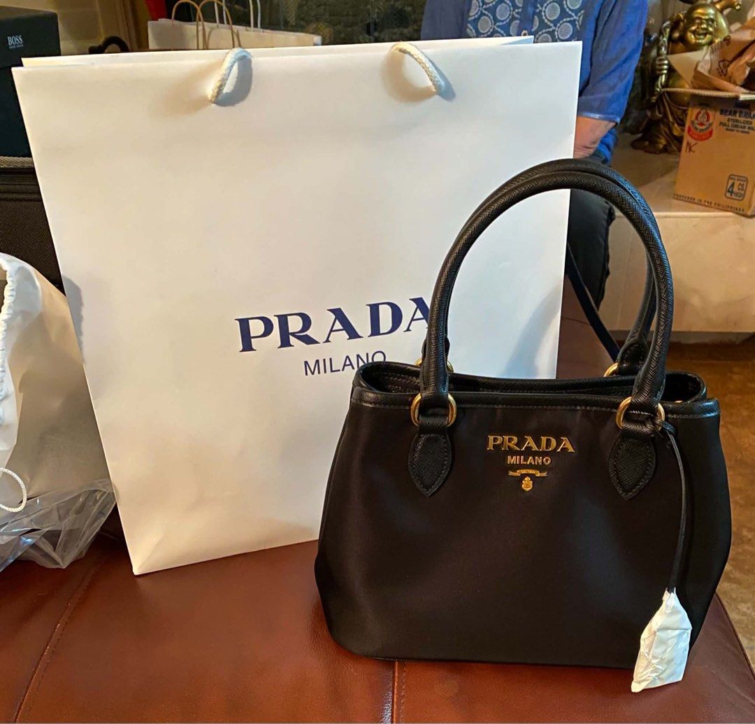 Authentic Prada Black Nylon Handbag Tessuto (Category: Luxury Bags & Wallets) located in Cabuyao City. Submitted by iheartyouxoxo (Listing ID 1464734084, Image 1). Description: - Authentic Prada black nylon handbag - Elegant gold hardware with signature lettering logo - Structured top handles and structured base - Clean exterior with a classic, timeless design - Includes original white Prada paper shopping bag with rope handles Complete inclusion