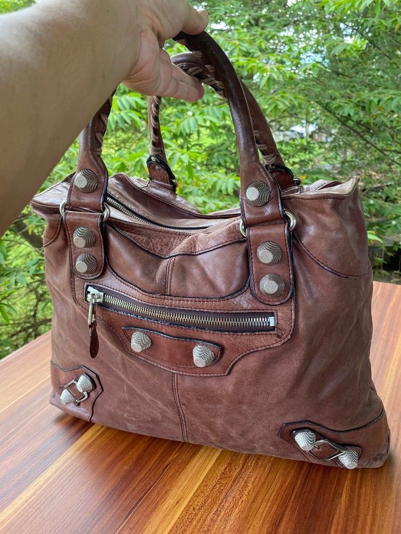 Balenciaga Brown Leather Studded Handbag (Category: Luxury Bags & Wallets) located in Bacacay. Submitted by jpbellen80790 (Listing ID 1464574204, Image 1). Description: -LAMPO ZIPPER BUT NOT CODED -PURE LEATHER - Stylish brown leather handbag - Accented with silver stud details - Features braided handles - Secure top zipper closure - Convenient front zipper pocket - Shows some signs of wear on bottom corners - Ideal for everyday use.