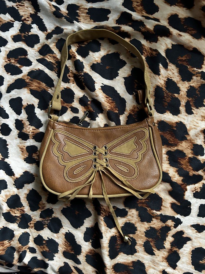 Brown Butterfly Lace-Up Shoulder Bag (Category: Shoulder Bags) located in Los Banos. Submitted by samsukehiro (Listing ID 1464579513, Image 1). Description: - Adorable brown shoulder bag - Features a charming butterfly design on the front - Stylish lace-up detail with ties - Adjustable strap for comfortable wear - Includes a main compartment and a small zip pocket inside - Versatile for everyday use or evening outings - Easily matches with variou