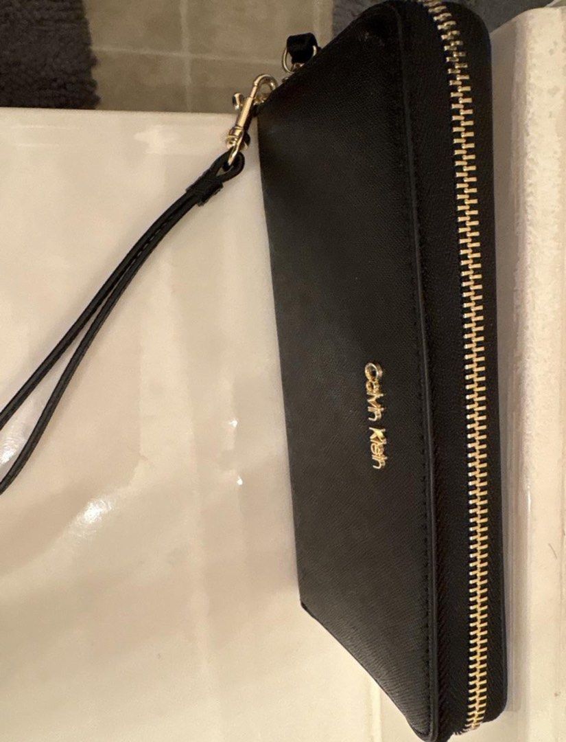 Calvin Klein Black Zip Around Wristlet Wallet (Category: Wallets & Card holders) located in Manila. Submitted by kaia_studios (Listing ID 1464702789, Image 2). Description: - Brand: Calvin Klein - Color: Classic Black with elegant Gold hardware and lettering - Material: Durable textured faux leather - Closure: Secure zip-around design - Features: Detachable wrist strap for versatile styling - Interior: Multiple card slots, slip compartments, and 