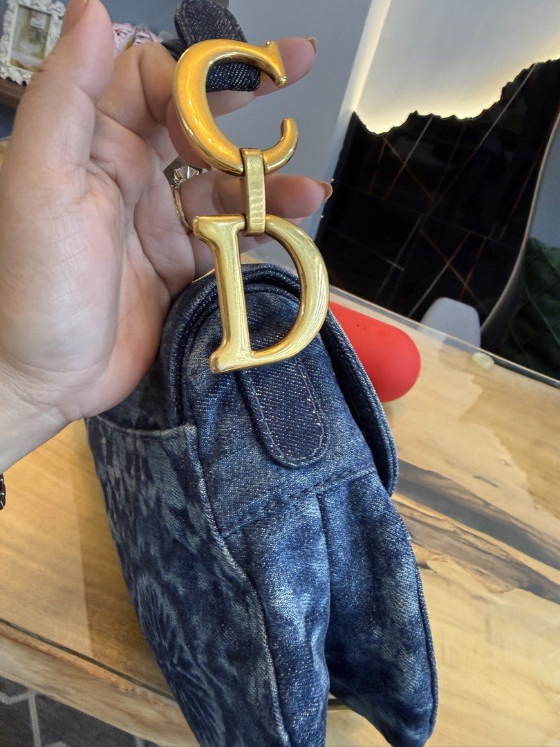 Christian Dior Denim Saddle Bag (Category: Luxury Bags & Wallets) located in Alfonso. Submitted by luxurose (Listing ID 1464758927, Image 3). Description: Christian Dior saddle bag in blue denim. Distinctive curved shape with the iconic hanging 'D' charm and 'CD' hardware on the strap attachments. Tie-dye or bleach wash pattern throughout with a circular motif on the back pocket. Short shoulder strap with contrast stitching. Clean hardware and de