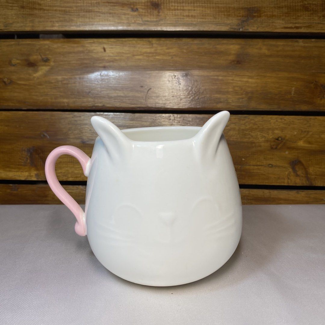 Cute Cat Ear Mug with Pink Handle (Category: Coffee & Tea Tableware) located in Quezon City. Submitted by oliviararo46032 (Listing ID 1464673849, Image 1). Description: - Adorable white mug shaped like a cat's face - Features cute pointy ears and a sweet smile - Lovely pastel pink handle - Ideal for morning coffee or tea - A fun addition to your kitchenware collection.