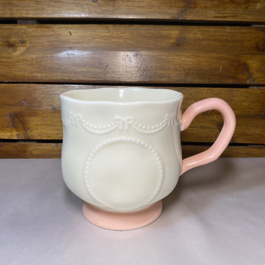 Cute Pink Ceramic Mug (Category: Coffee & Tea Tableware) located in Quezon City. Submitted by oliviararo46032 (Listing ID 1464673593, Image 1). Description: - Adorable white ceramic mug - Features a lovely embossed ribbon and circle design - Soft pink handle and base - Perfect for coffee or tea - Makes a great gift - Approximately 4 inches tall.