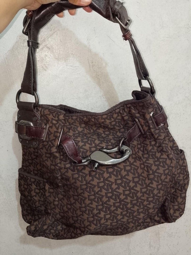DKNY Brown Monogram Shoulder Bag (Category: Luxury Bags & Wallets) located in Santo Tomas. Submitted by noviemolde07815 (Listing ID 1464734138, Image 1). Description: - Brand: DKNY - Style: Shoulder bag - Material: Brown monogram fabric with dark brown leather handles - Hardware: Dark brown accents with front clasp and side buckle details - Interior: Dark lining with DKNY branded pockets and Made in China tag - Capacity: Spacious enough for every