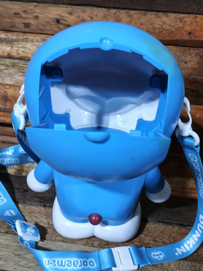 Doraemon Popcorn Bucket with Strap (Category: Character Goods) located in San Jose del Monte. Submitted by toys.merch.electronic (Listing ID 1464696716, Image 2). Description: - Official Dunkin' Doraemon collaboration popcorn bucket - Adorable winking expression, red nose, yellow bell, and white belly pocket - Pop-open head design to store snacks, candies, or small items - Includes original blue strap with 'Doraemon and Dunkin' text and functiona