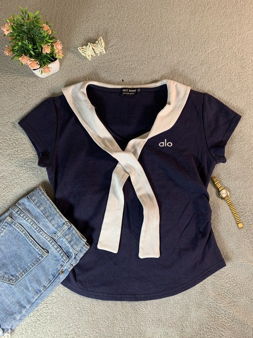 First Sight Navy Sailor Collar Top with Alo Logo (Category: Blouses) located in Candelaria. Submitted by angeltesoro3110 (Listing ID 1464675702, Image 1). Description: - Navy blue short-sleeved top - White sailor collar with tie detail - Small 'alo' logo embroidered on chest - Side ruching for a flattering fit - Ideal for casual or preppy style.