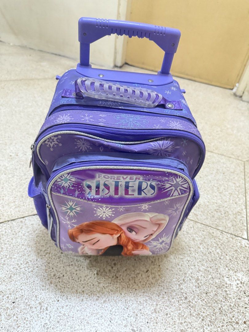 Frozen trolly school bag (Category: Backpacks) located in Bocaue. Submitted by cocro_crafts (Listing ID 1464571413, Image 2). Description: - Features Elsa and Anna from Disney's Frozen with a 'Forever Sisters' graphic. - Versatile design with wheels, a retractable handle, and adjustable shoulder straps. - Includes side mesh pockets for easy access to water bottles. - Ideal for school, day trips, or travel adventures. - See picture for flaws .