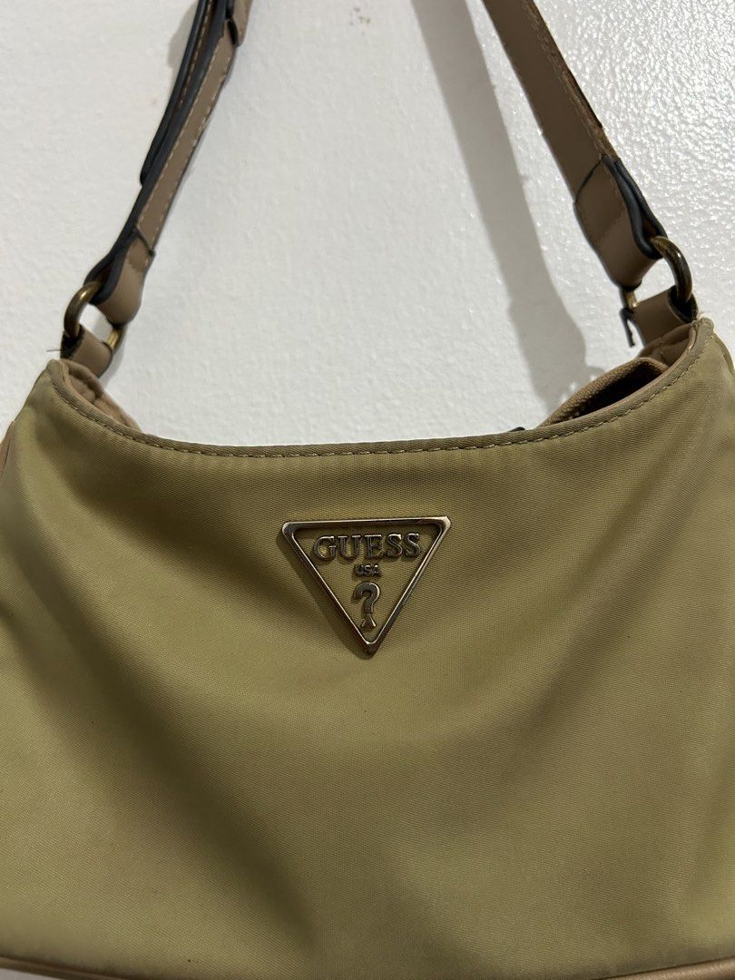 Guess Khaki Nylon Shoulder Bag (Category: Shoulder Bags) located in Angeles City. Submitted by cassey_phoenix (Listing ID 1464707735, Image 2). Description: - Brand: Guess - Color: Khaki olive with tan faux leather trim - Material: Durable nylon body - Hardware: Gold-tone - Logo: Metal triangular Guess USA plaque on the front - Closure: Zip top closure - Interior: Branded fabric lining with one zippered pocket - Strap: Adjustable - Condition: Cle