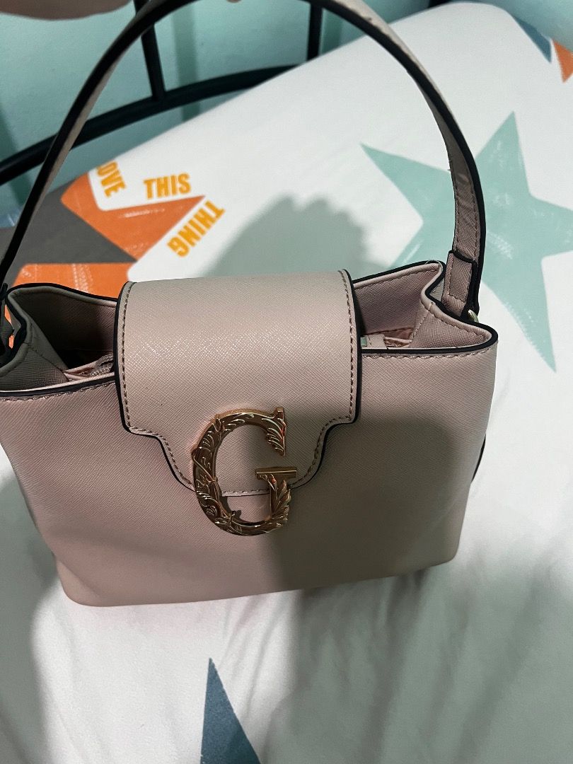Guess Roseburg Small Satchel (Clay) (Category: Purses & Pouches) located in Consolacion. Submitted by hann_m_m (Listing ID 1464760022, Image 3). Description: Brand/Model: Guess Roseburg Small Satchel Color: Clay (dusty pink/beige neutral shade) Design: Structured small handbag featuring a prominent ornate 'G' logo on the front flap Handle: Sturdy single top handle for easy carrying Interior: Fully lined with a secure zippered pocket and slip comp