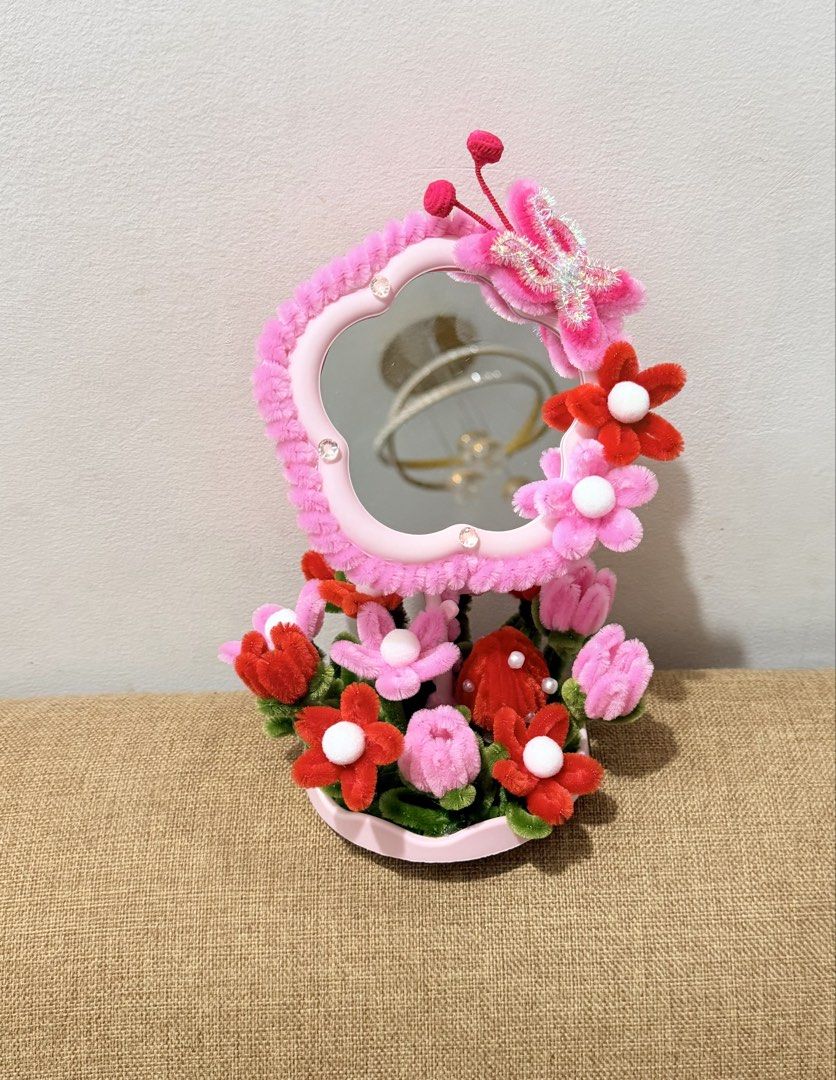 Handmade Pipe Cleaner Flower Desk Mirror (Category: Mirrors) located in Dasmarinas. Submitted by ligean2738954 (Listing ID 1464724886, Image 3). Description: Custom handmade vanity mirror decorated with fluffy pipe cleaner flowers and butterfly accents. Available in two colorways: purple or pink and red. Stands securely in a white scalloped base. Cute decor piece for a vanity table, desk, or bedside table. Bright and cheerful room accessory..