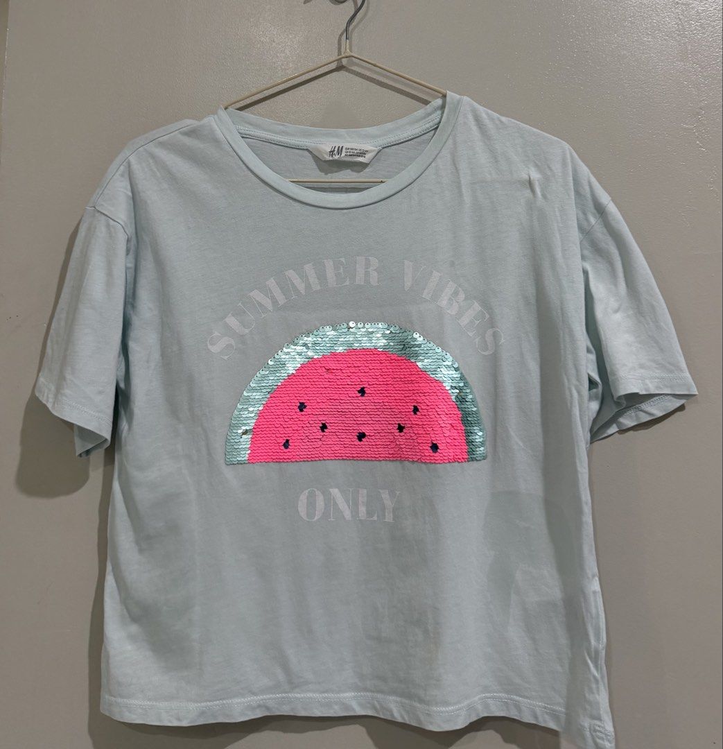 H&M Top 12-14Y (Category: Babies & Kids Fashion) located in Subic. Submitted by kittysclosetsale (Listing ID 1464746397, Image 1). Description: - Brand/Style: H&M light blue short-sleeve tee - Design: Fun sequin watermelon graphic with 'Summer Vibes Only' text - Size: EUR 158/164 (Fits US 12-14Y) - Fit: Relaxed and comfortable - Material: Soft cotton fabric, great for warm weather - Easy to pair with jeans or shorts for casual wear.